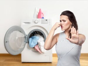 lavatrice aperta con bucato che fuoriesce e donna che si attappa il naso