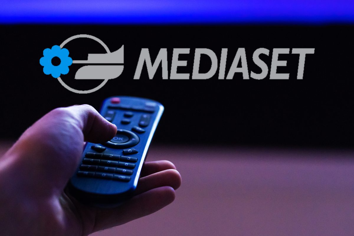 mano di un uomo con un telecomando e logo Mediaset sullo sfondo
